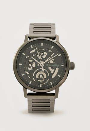 Calvin Klein schwarze und silberne Metall-Armbanduhr mit Skelettzifferblatt, drei Hilfszifferblättern und silbernen Stundenmarkierungen auf einem Metallgliedband.