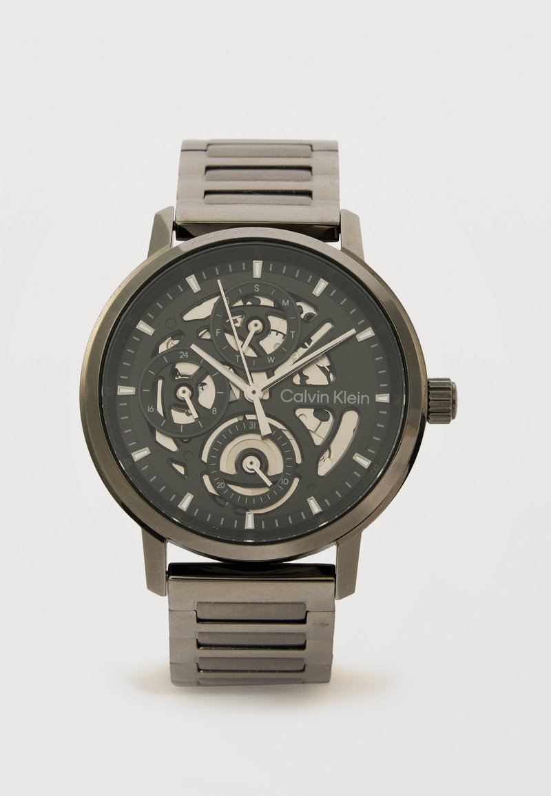 Μαύρο και ασημί μεταλλικό ρολόι χειρός Calvin Klein με καντράν σκελετού, τρεις υποκαντράν και ασημένιους δείκτες ώρας σε μεταλλικό λουράκι με κρίκους.