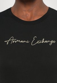 Zwarte katoenen t-shirt met een gouden strass-logo, "Armani Exchange," in cursief schrift op de borst, met een ronde halslijn.