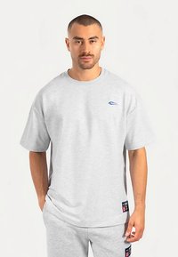 Grå bomuld T-shirt med korte ærmer, rund halsudskæring og blåt logo på brystet. Har en afslappet pasform og detaljer med sidelabel.