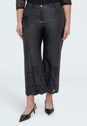 Sorte bukser med vidde ben og blomsterlaserudskæring nær kanten, båret med sorte spidse slingback-hæle og en sort blondebluse.