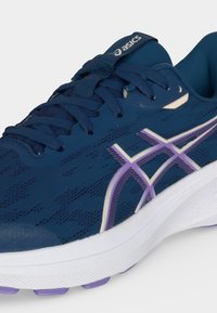 Ναυτικό μπλε παπούτσι για τρέξιμο Asics με μωβ και λευκό λογότυπο, χοντρή λευκή σόλα και ναυτικό μπλε κορδόνια.