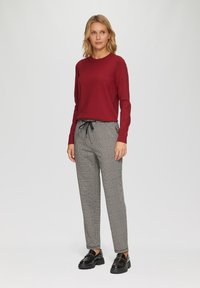 Rode, lange mouw gebreide trui gecombineerd met grijze geblokte broek met een elastische tailleband. Zwarte instappers maken de outfit compleet.