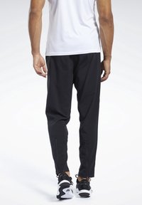 Černé sportovní kalhoty s užším střihem, se zipovými kotníky a lehkým materiálem. Nosené s černobílými teniskami.