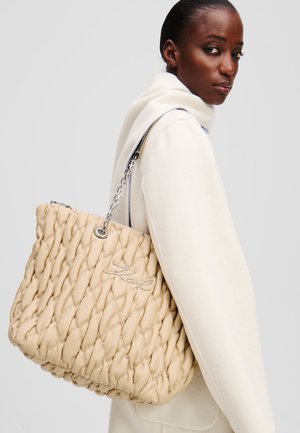Borsa a spalla beige intrecciata con un design trapuntato, hardware argentato e un dettaglio con logo. Presenta una tracolla in catena per un facile trasporto.