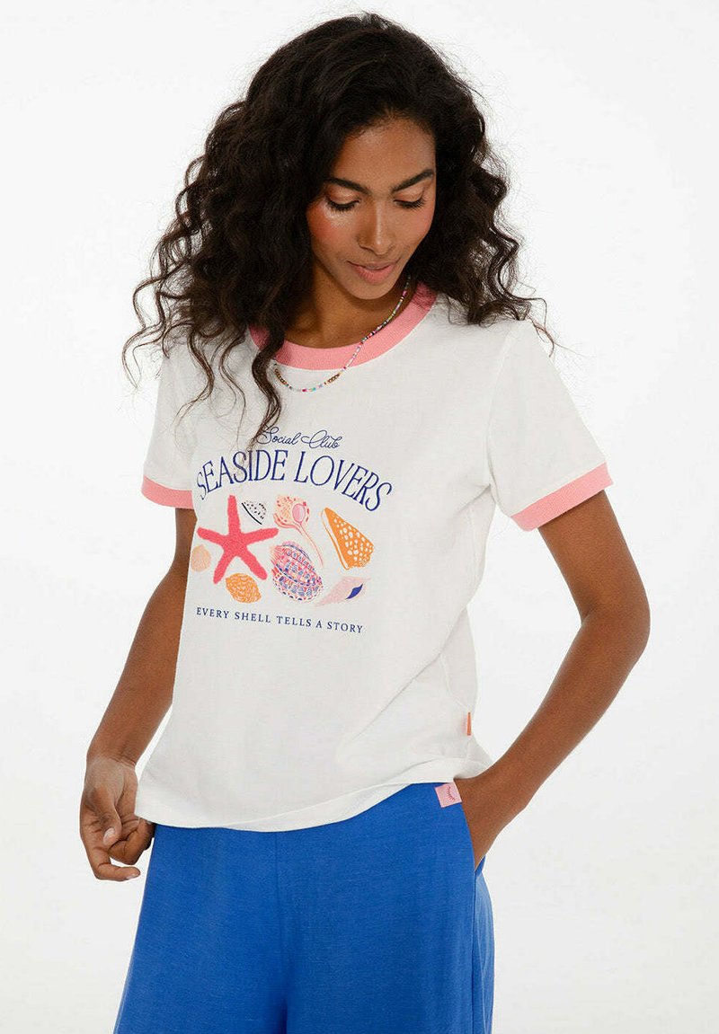 Bílý tričko s krátkým rukávem a růžovými akcenty. Na přední straně se nachází grafika "Seaside Lovers" se skořápkami a hvězdicemi; volný střih, měkký bavlněný materiál.