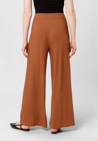 Brederaad bruine broek heeft een geribbelde textuur en een elastische tailleband. De stof lijkt zacht en hangt losjes, wat het comfort benadrukt.