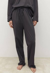 Tmavě šedé tepláky vyrobené z měkké látky, s elastickým pasem na šňůrku a volným střihem, doplněné o odpovídající vršek.