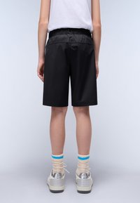 Pantaloni corti neri con elastico in vita, lunghi fino al ginocchio, realizzati in tessuto leggero. Abbinati a sneakers beige e calzini a righe pastello.