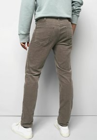 Brown corduroy pants with a slim fit, featuring two back pockets and a textured surface, paired with white sneakers.