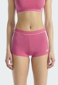 Femme portant un short de sport rose et un crop top assorti, se tenant devant un fond clair.