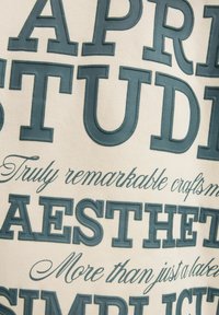 Textile featuring raised, dark teal lettering on a light beige background, with various typographic styles and phrases. Smooth fabric texture.