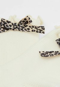 Cremefarbene, gerippte Socken mit einem rüschierten oberen Rand und schwarzen Leopardenmuster-Schleifen als Akzenten. Weicher Stoff mit enge Passform.