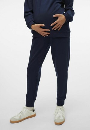 Tiefblaues Schwangerschafts-Trainingsanzug-Oberteil und schmal geschnittene Hose aus weichem Material, mit lockerer Passform und gerippten Bündchen, kombiniert mit weißen Sneakers.