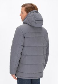 Jachetă puf gri cu glugă, având un design cusut și cusături ribbate. Textură moale și croială de lungime medie, cu buzunare laterale.