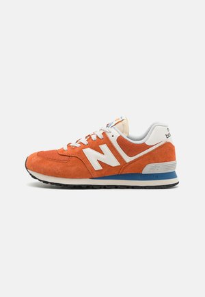 Orange suede sneaker with white and grey accents, featuring a padded collar, logo on the side, and a black rubber outsole.