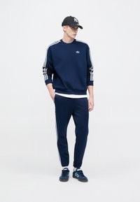 Μπλε σκούρο φούτερ και φόρμα με λευκές ρίγες στα πλάγια. Συνδυασμένα με καπέλο με ασπρόμαυρες ρίγες και μπλε σκούρα αθλητικά παπούτσια.