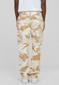 Beige camo cargo pants with side pockets, straight-leg design, and soft cotton material. Features a relaxed fit and subtle textured pattern.