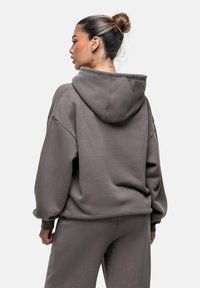 Hoodie grigia oversize realizzata in tessuto morbido, caratterizzata da un ampio cappuccio, spalle scese e polsini a coste. Texture liscia, design minimalista.