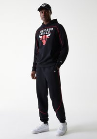 Svart hettegenser med røde detaljer som har "CHICAGO BULLS"-logo, kombinert med svarte joggebukser og hvite joggesko. Enkelt, komfortabelt treningstøy.