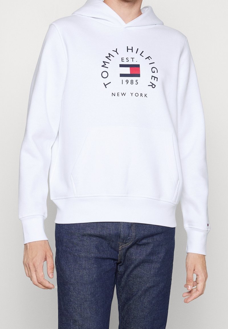 Weißer Hoodie mit einer vorderen Tasche, gerippten Bündchen und einem Logo mit blauen, roten und schwarzen Akzenten. Geschmeidige Textur und lässige Passform.