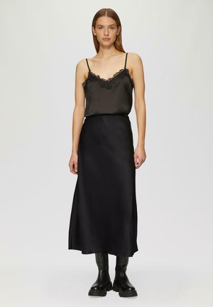 Zwarte satijnen camisole met kantafwerking, gecombineerd met een zwarte satijnen rok. De outfit heeft een vloeiende silhouet en wordt aangevuld met zwarte chunky laarzen.