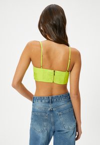 Bralette de encaje verde neón con tirantes ajustables, cierre de cremallera en la parte posterior y diseño ajustado, combinado con vaqueros de cintura alta azul.