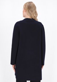 Cardigan blu navy con maniche lunghe, colletto a punte e taglio dritto. Tessuto morbido con una finitura liscia, senza motivi visibili o accessori.