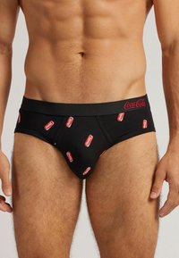 Schwarze Slips mit Coca-Cola-Logo-Druck in Rot, mit einem elastischen Bund, der den Markennamen in roter Schreibschrift zeigt. Weicher Stoff.