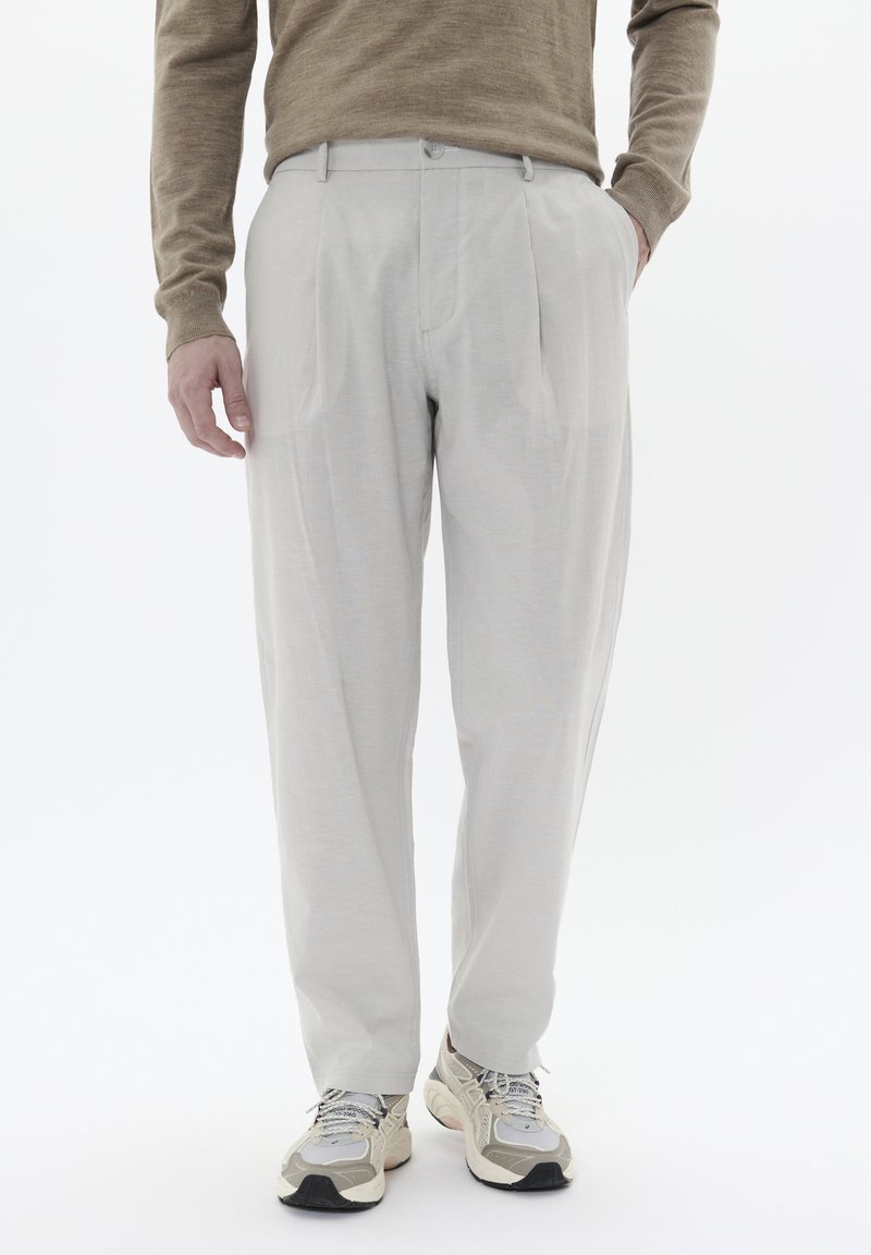 Pantalones gris claro de una tela suave, con un frente plisado, lazos para cinturón y un corte relajado. Combinados con zapatillas de tonos neutros.