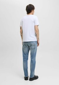 Camiseta blanca de algodón combinada con jeans de denim azul claro. Los jeans tienen un corte clásico con bolsillos y un ligero desgaste. Unos zapatos negros completan el conjunto.