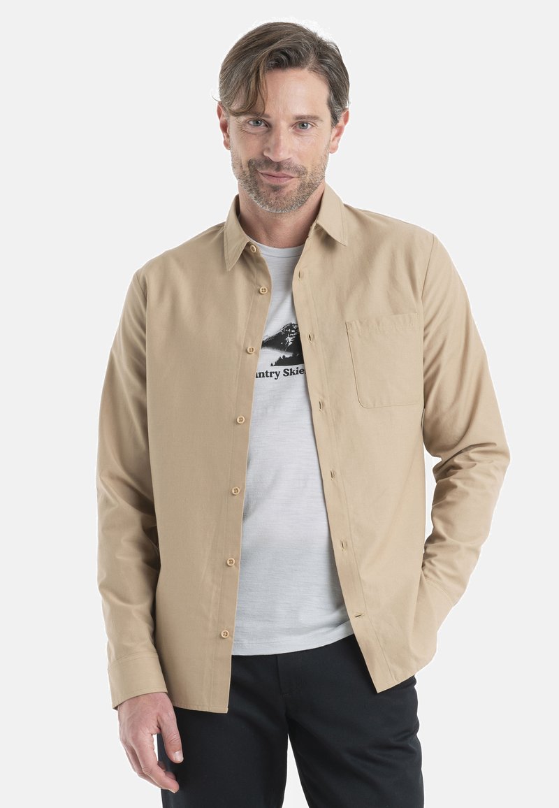 Beige skjorta med knappar i lätt material, med en bröstficka, långa ärmar och klassisk krage, bärs över en ljus t-shirt.