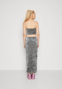 Šedý dvoudílný outfit složený z crop topu s tenkými ramínky a sukně až na zem. Texturovaná tkanina s pomačkaným vzhledem; doplněno růžovými botami.