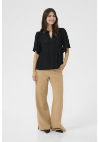Blusa a righe nere con scollo a V e maniche corte a sbuffo, abbinata a pantaloni beige a gamba larga e scarpe nere con punta.