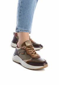 Zapatillas deportivas marrones y beige con texturas mixtas, que cuentan con un sistema de cordones destacado, detalle de logotipo y una suela blanca gruesa.