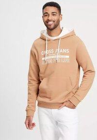 Brązowy hoodie z białymi sznurkami i przednią kieszeni ą. Posiada napis "CROSS JEANS" w białym kolorze. Noszony z białymi spodniami dla kontrastu.