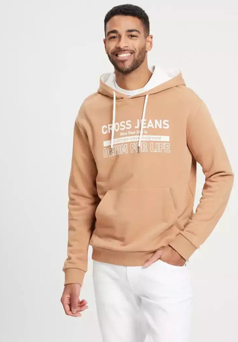 Brązowy hoodie z białymi sznurkami i przednią kieszenią. Posiada napis "CROSS JEANS" w białym kolorze. Noszony z białymi spodniami dla kontrastu.