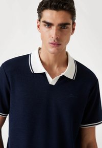 Polo de color azul marino con un collar blanco que presenta rayas en azul marino. Tejido texturizado con un discreto bordado del logo en el pecho.