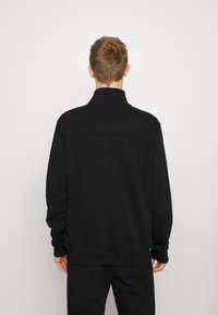 Sort sweatshirt med høj krave, lange ærmer og ribbede manchetter. Lavet af glat, blødt stof; har en diskret detalje med bagsøm.