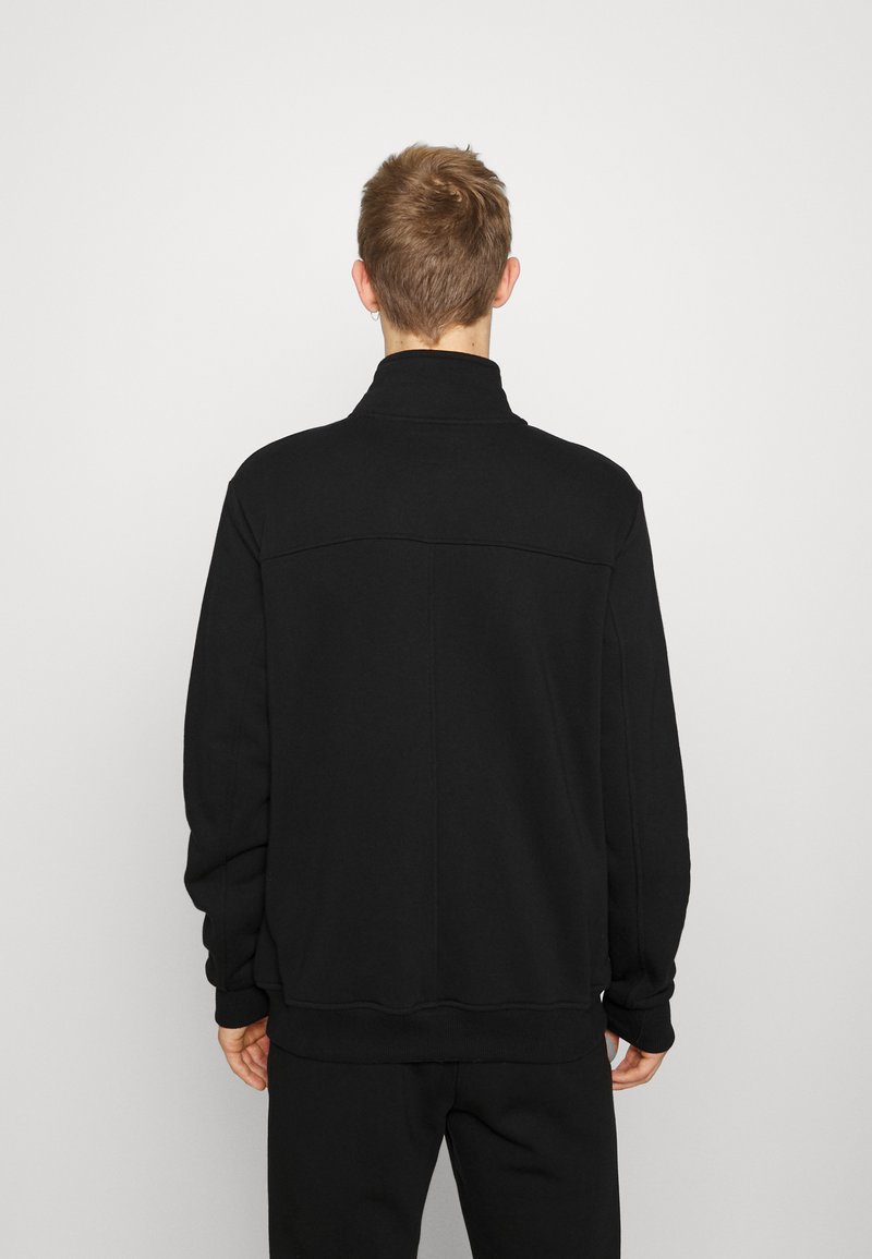 Black sweatshirt with high collar, long sleeves, and ribbed cuffs. Made of smooth, soft fabric; features a subtle back seam detail.
