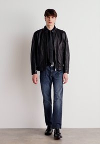 Black leather bomber jacket, fitted with zip closure, paired with dark denim jeans and black shoes. Simple design, no patterns.