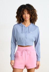 Sudadera recortada de color azul claro con cremallera, fabricada en tejido de malla y con capucha. Combinada con unos suaves pantalones cortos rosas con cordón.