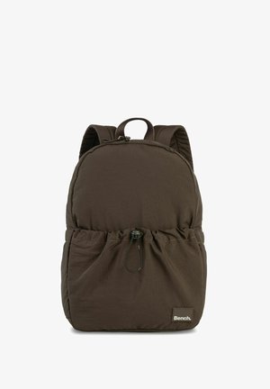Brown nylon backpack with a rounded shape, drawstring closure at the base, and a logo tag. Features padded shoulder straps and a top handle.