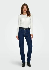 Vit ribbad långärmad topp och blå denimjeans med ett svart bälte. Rakt ben-design och slät textur, med minimala sömnadsdetaljer.