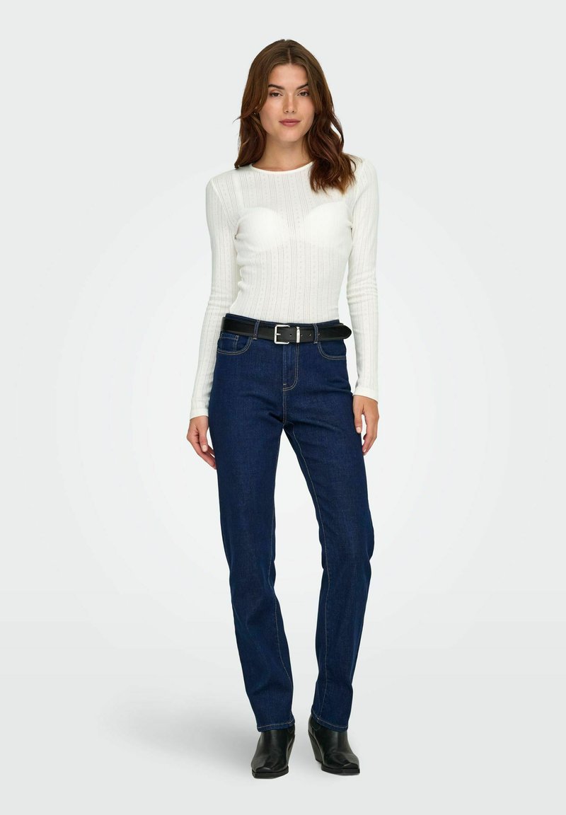 Vit ribbad långärmad topp och blå denimjeans med ett svart bälte. Rakt ben-design och slät textur, med minimala sömnadsdetaljer.