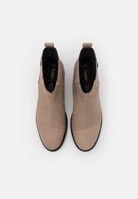 Par de zapatos TOMS beige sin cordones con suelas negras, costuras visibles y paneles laterales elásticos, mostrados desde arriba sobre un fondo blanco.
