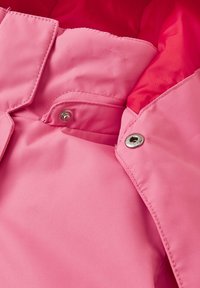 Giacca rosa con un tessuto liscio e strutturato. Presenta hardware a pressione argentato e un rivestimento interno a contrasto. Vista ravvicinata del colletto e dei ganci.