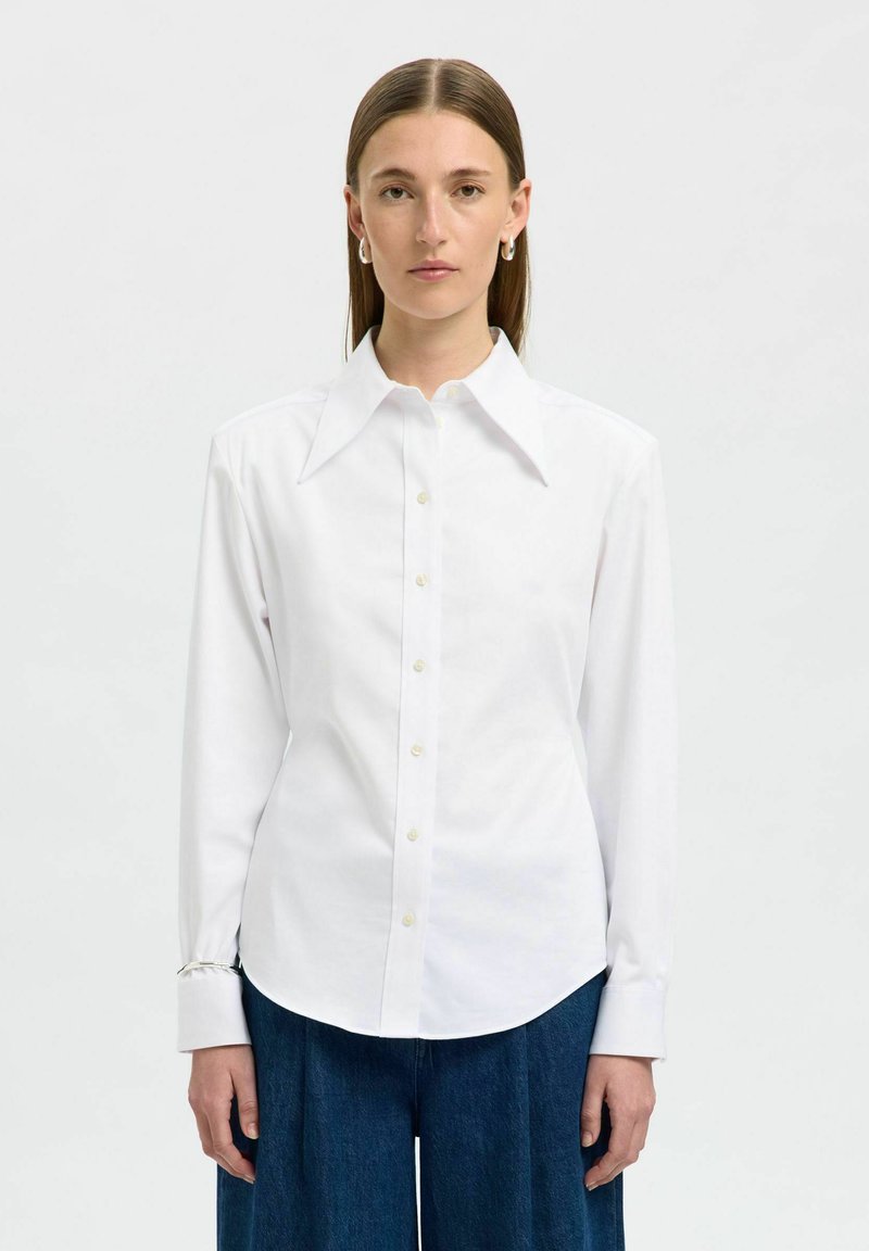 Camicia bianca con colletto ampio e maniche lunghe, caratterizzata da dettagli ai polsini e orlo arrotondato, realizzata in tessuto rigido.
