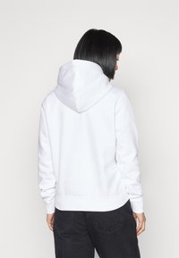 Felpa bianca con cappuccio realizzata in un mix di cotone. Presenta una tasca a marsupio e polsini a costine. Tessuto morbido, vestibilità rilassata, con un ampio cappuccio.