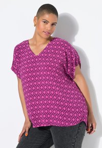 Blusa magenta a V con motivo geometrico a diamante, maniche corte e vestibilità ampia. Abbinata a jeans in denim scuro. Texture del tessuto liscia.